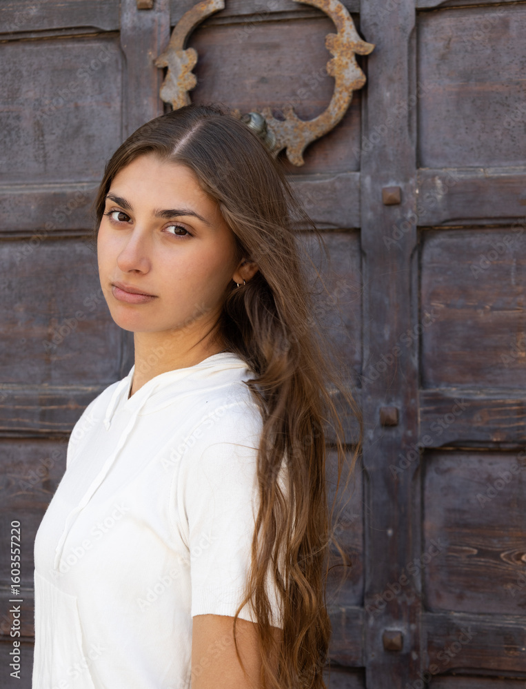 Fototapeta premium Portrait of young woman in white top against rustic wooden door.