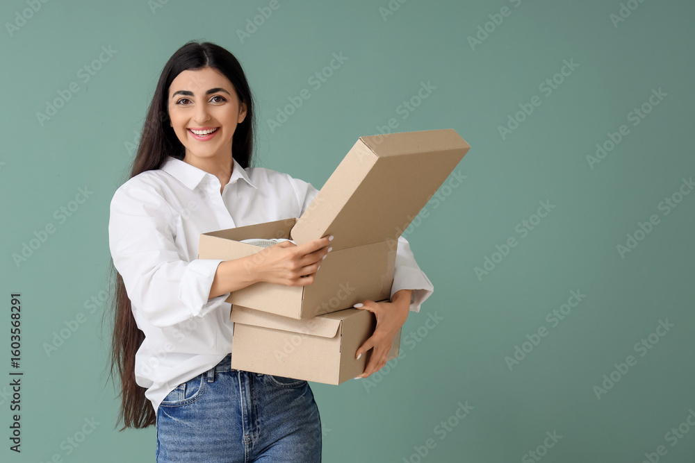Fototapeta premium Young woman holding wardrobe boxes on green background