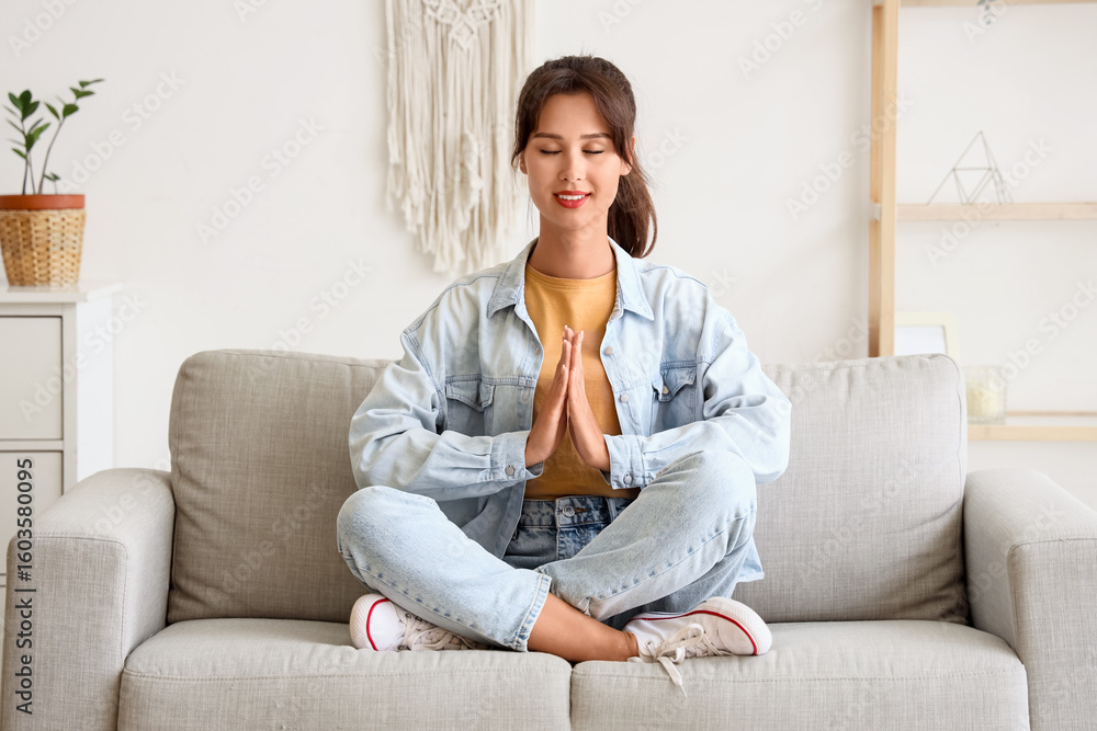 Young woman meditating on sofa at home Young woman meditating on sofa at home
