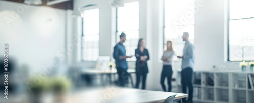 Four people stand talking near a window in a bright office space.