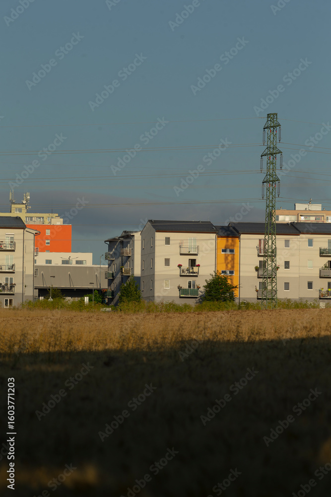 Fototapeta premium In the foreground, a wide and open field stretches out, leading to a row of modern apartment buildings that create an urban landscape