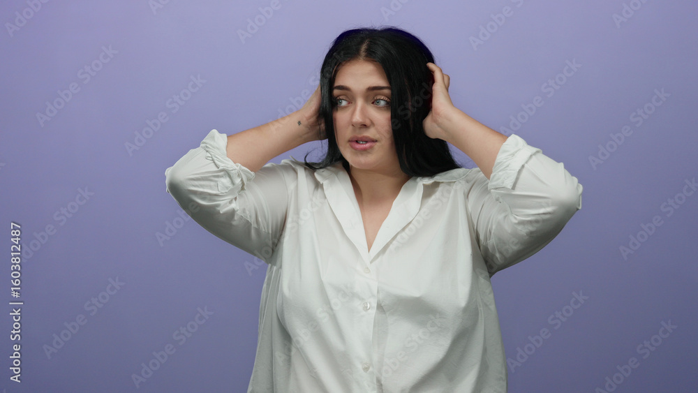 Woman with hands over ears stands against a purple wall, expressing frustration in a white shirt; plus size young lady isolated over plain background, conveying emotion and body positivity. Woman with hands over ears stands against a purple wall, expressing frustration in a white shirt; plus size young lady isolated over plain background, conveying emotion and body positivity.
