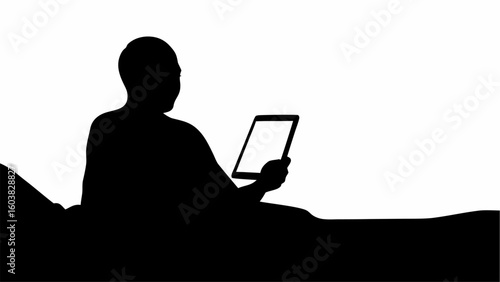 Silhouette of a person sitting in bed and holding a tablet with a blank screen in their hand reading it