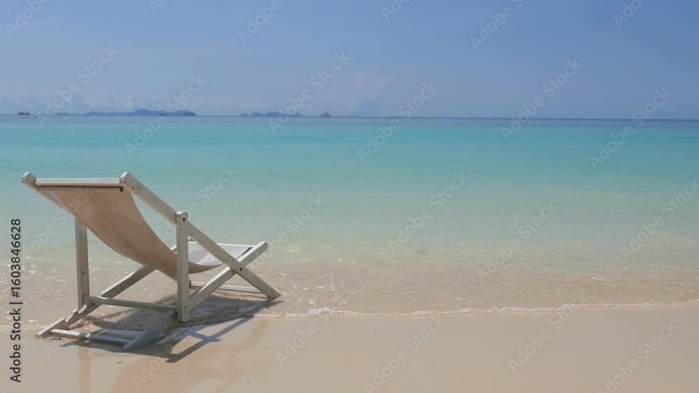 An empty deck chair rests at the water's edge on a serene tropical beach. An empty deck chair rests at the water's edge on a serene tropical beach.