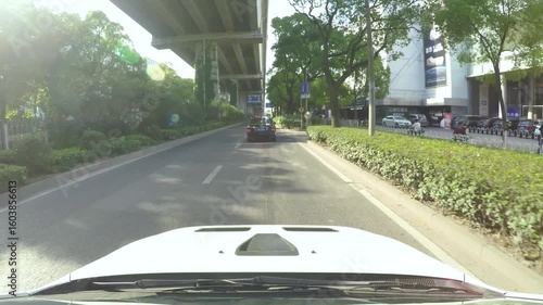 Driving through a vibrant urban area with greenery and commercial buildings during the day