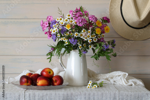 Summer still life with wildflowers in a white jug and peaches on a table