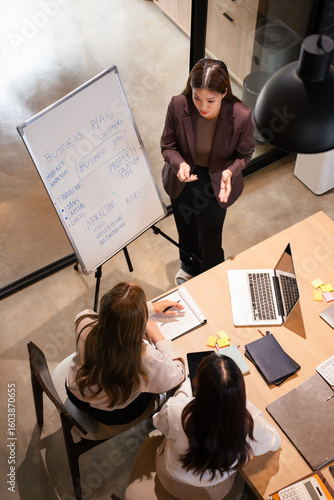 Confident mature business professional woman talking to younger female colleague at office table, speaking, gesturing, teaching, explaining work tasks. Elder mentor training intern.