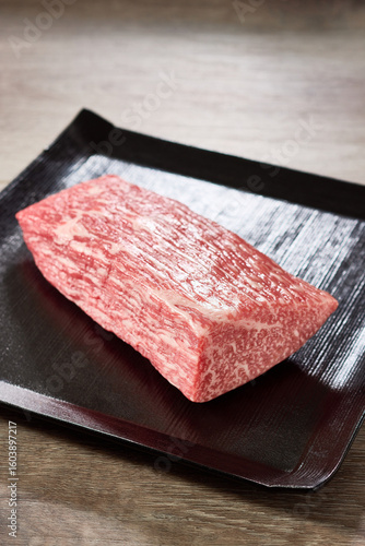 A5ランク黒毛和牛のもも肉ブロックを黒い角皿に盛り付けた高級感あふれる食材写真。繊細な霜降りと赤身の旨味が魅力の5等級和牛。日本料理や精肉広告に最適なイメージ。