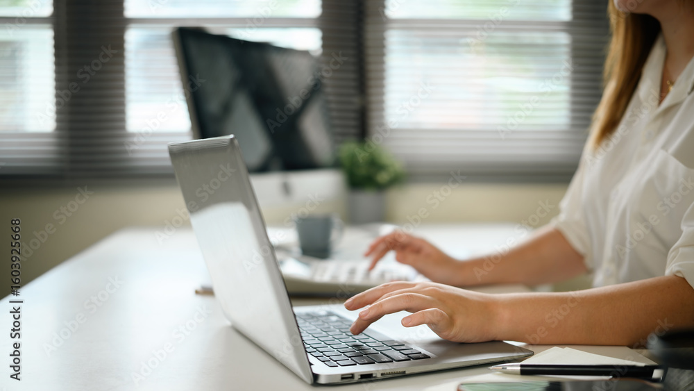 Fototapeta premium Close-up of female hands typing on a laptop keyboard at a modern workspace with natural light