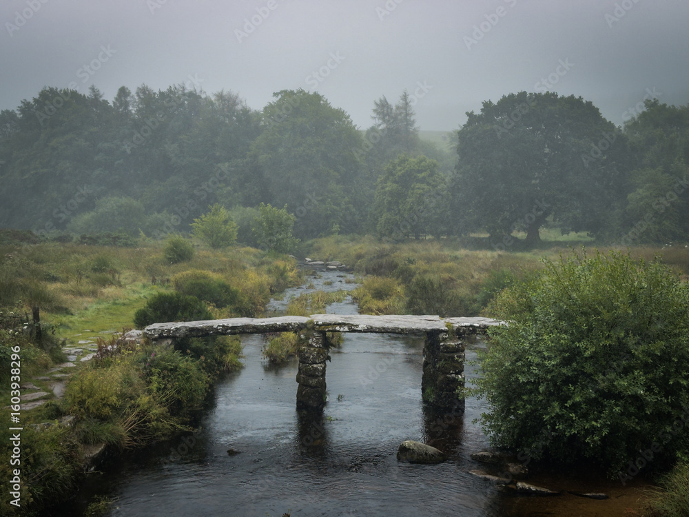 Obraz premium Postbridge Clapper Bridge over the East Dart River on a foggy and rainy day in Darmoor national park, Devon, England.