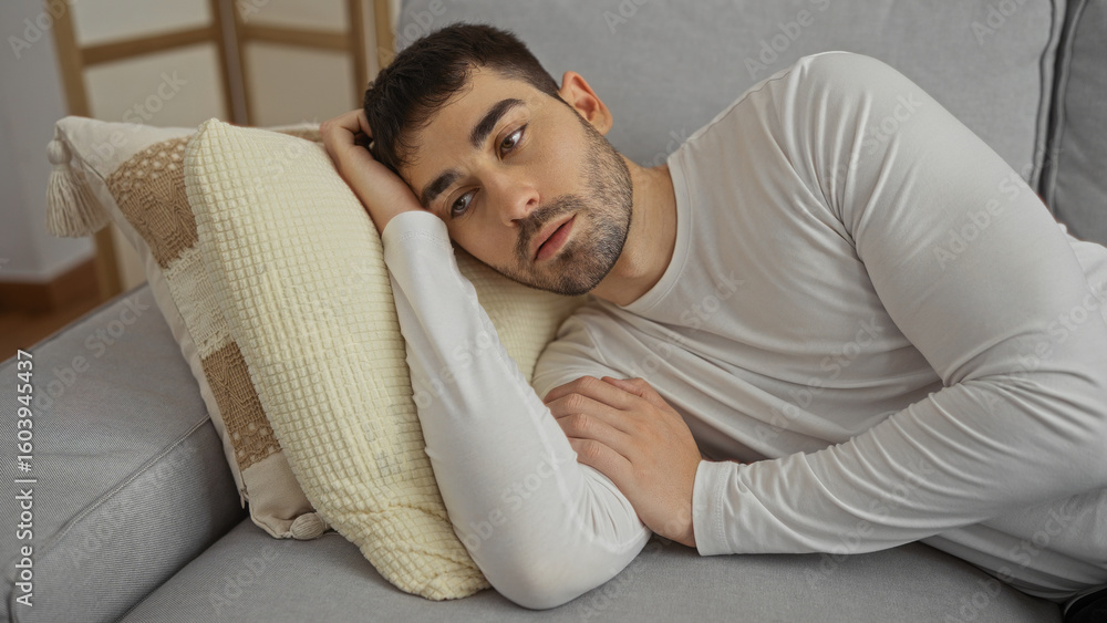 Young man relaxing indoors on a comfortable sofa, exuding a sense of calm and contemplation in a stylish, modern living room setting. Young man relaxing indoors on a comfortable sofa, exuding a sense of calm and contemplation in a stylish, modern living room setting.
