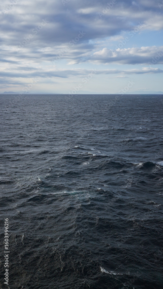 Fototapeta premium Expansive ocean with choppy waves under a partly cloudy sky, suggesting a serene yet dynamic seascape on the horizon.