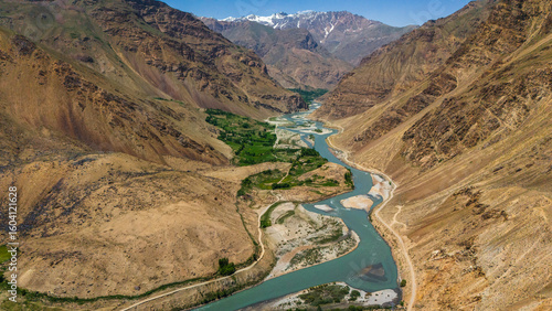 Aerial view of the Wakhan Valley, Pamir Mountains, Tajikistan. The Panj River winding between rugged peaks and green villages along the remote Afghan border