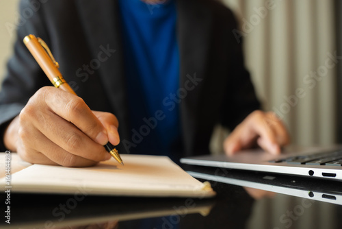 Photography man sitting at a table at home working on a laptop and writing down ideas in a notebook