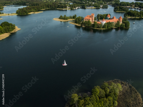 Aerial view of Trakai Island Castle, a medieval castle, stands in stark contrast to the dark water, with a lone sailboat nearby, Trakai, Vilnius country, Lithuania.