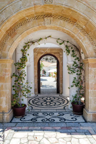 Ornate Entryway of Lardos Monastery with Stone Mosaic and Lush Plant Arch
