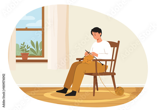 A young man sits on a wooden chair by a window, calmly knitting with yellow yarn.