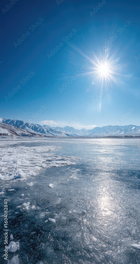 Fototapeta premium Frozen lake under a bright blue sky, snowy mountains in the background