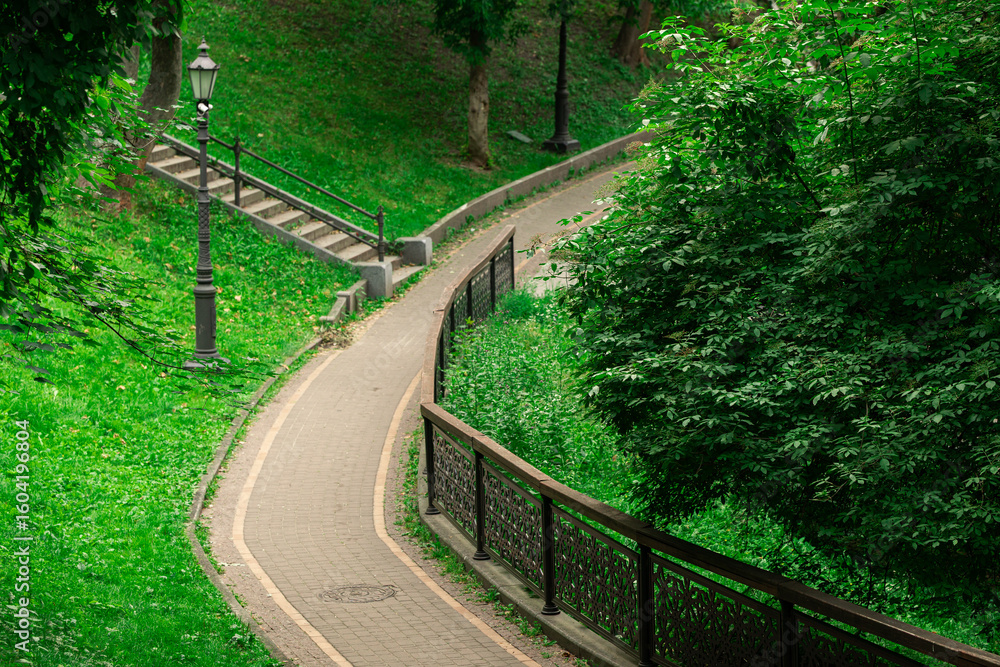 Obraz premium park outdoor scenery walking site paved road track curved shape in green trees and grass hills environment space of landscaped design place