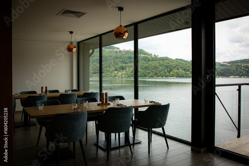 A modern restaurant interior with large windows showcasing a beautiful lake and green hills