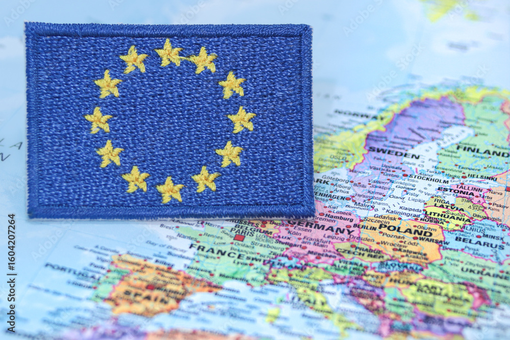 Naklejka premium Embroidered European Union flag made from thread and cloth, positioned over Europe on a world map. Represents global diplomacy, eco travel and EU identity.