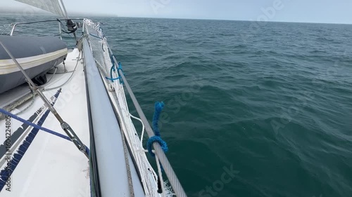 Looking ahead from down the side of a sailing yacht running downwind across calm seas in light airs.