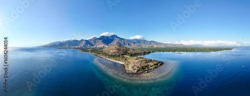 Aerial view of dramatic mountains meeting the serene ocean, with a sunlit peninsula, Pemuteran, Bali, Indonesia.