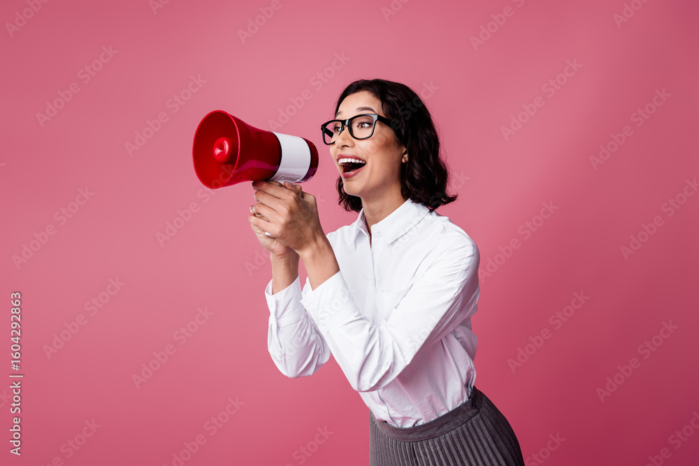 Joyful businesswoman with megaphone making announcement dressed in formal attire against vibrant pink background Joyful businesswoman with megaphone making announcement dressed in formal attire against vibrant pink background