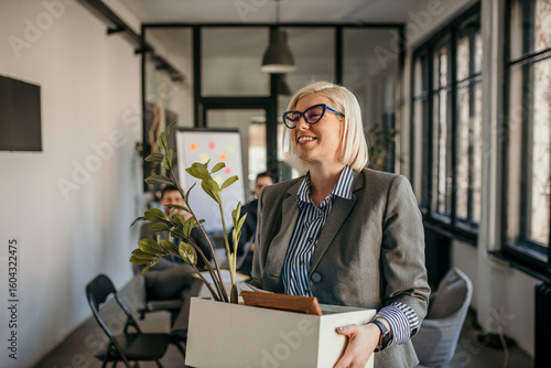 Bilde på lerret Smiling businesswoman leaving office carrying box with belongings