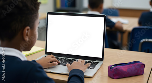 African junior school kid girl student using laptop computer with white blank empty mockup screen at desk in classroom. Online education class software website tech ads concept. Over shoulder view