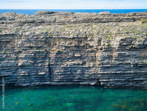 A stunning view of stratified rock formations at Bridges of Ross, Ireland, with clear blue waters below.