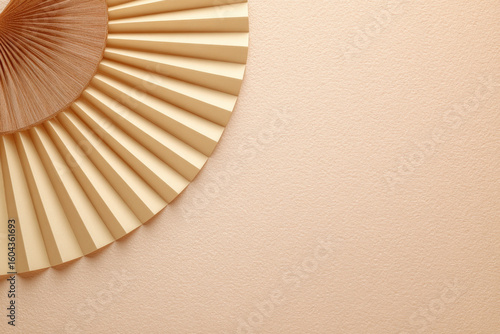 Pleated paper fan shape in beige color against soft peach background creates serene and elegant atmosphere