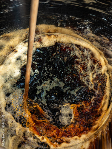 A dark liquid with frothy bubbles and swirls stirred with a wooden paddle