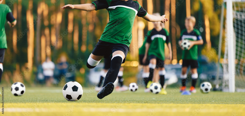 Fototapeta premium Youth Soccer Game in Progress. Boys in Green Jerseys Practicing Football on Outdoor Field. Junior Football Match and Training Session