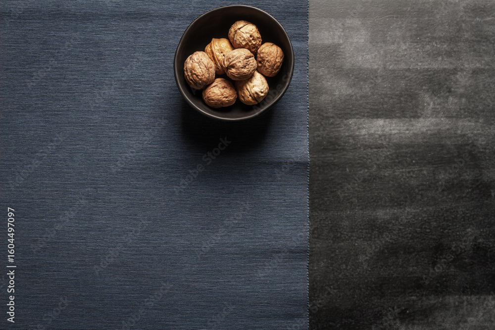 Fototapeta premium Black bowl with walnuts and blue table cloth on black chalkboard background. Flat lay. Top view.
