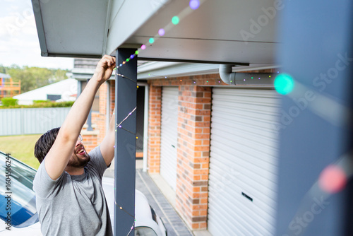 Man stringing up smart fairy lights at front of house for christmas