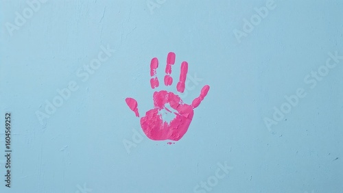 A young kid's hand dipped in pink paint creating a print on a blue background.