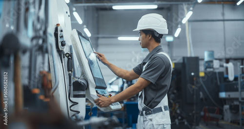 Fototapeta Asian Male Engineer in a White Hard Hat Operating a CNC Milling Machine in a Modern Factory