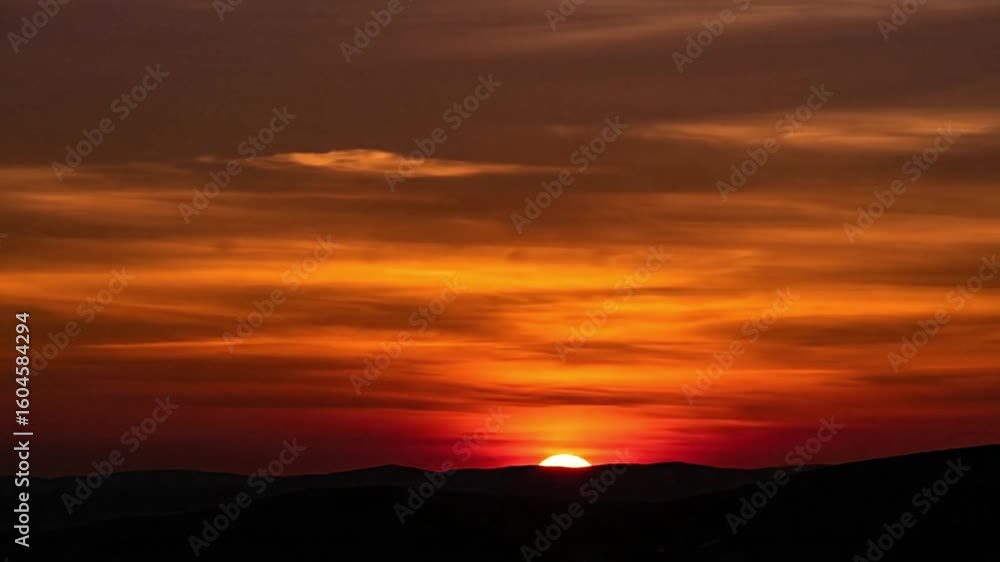 An orange sunset over dark silhouettes of rolling hills or dunes An orange sunset over dark silhouettes of rolling hills or dunes