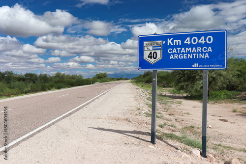 A blue road sign indicates distance and direction on the iconic Route 40, pointing to Km 4040 towards Catamarca, Argentina, under a partly cloudy 