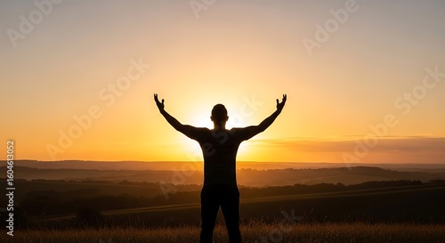 Silhouette of a man with arms raised towards the sun during sunset, overlooking a landscape with rolling hills.