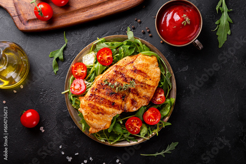 Grilled chicken breast with arugula and tomatoes i a plate and black background top view