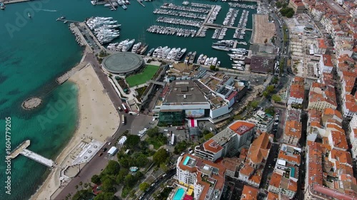 Top‑down drone shot of Cannes’ Palais des Festivals with the red carpet ready, La Croisette beach and a packed superyacht marina on the turquoise Mediterranean, France.