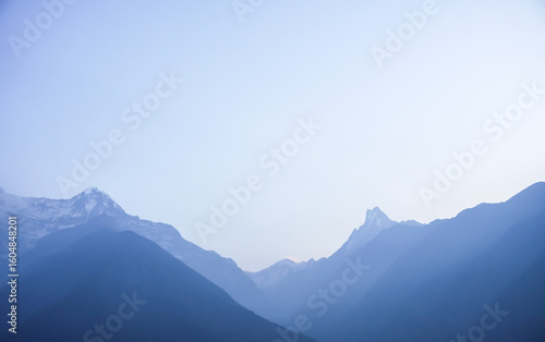 Fototapeta Naklejka Na Ścianę i Meble -  Snow-capped Mount Annapurna peaks visible in the morning with ray of light and mist at Annapurna Base Camp, Nepal with blue sky and white clouds background.