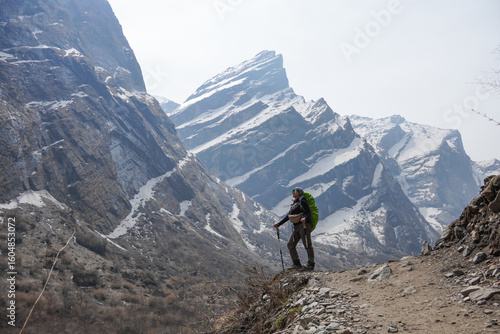 Young asian female hiker carrying mountain backpack and using trekking pole took photos after successfully hiking to Annapurna Base Camp, with the snow-capped Himalayan peaks visible in the morning