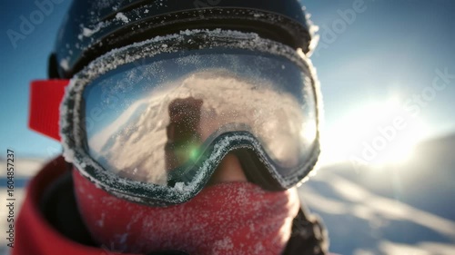 Close-up of skier's head in goggles with frost forming around edges and hands adjusting straps in sunlight.