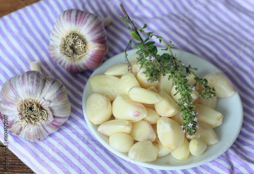 Freshly peeled garlic cloves and thyme on the small plate. Top view of garlic cloves and bulbs on the table.