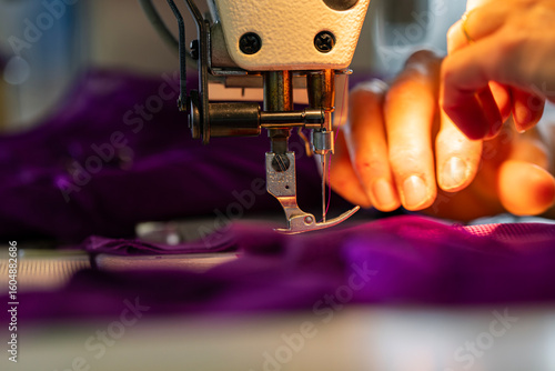 Zoom sur une machine à coudre en fonctionnement avec des mains en pleine action guidant le tissu, illustrant le geste précis de la confection artisanale.