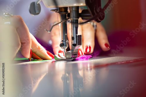 Schilderij op canvas Zoom sur une machine à coudre en fonctionnement avec des mains en pleine action guidant le tissu, illustrant le geste précis de la confection artisanale