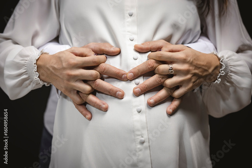 Hands of expecting couple on pregnant belly – close-up maternity and parenthood concept